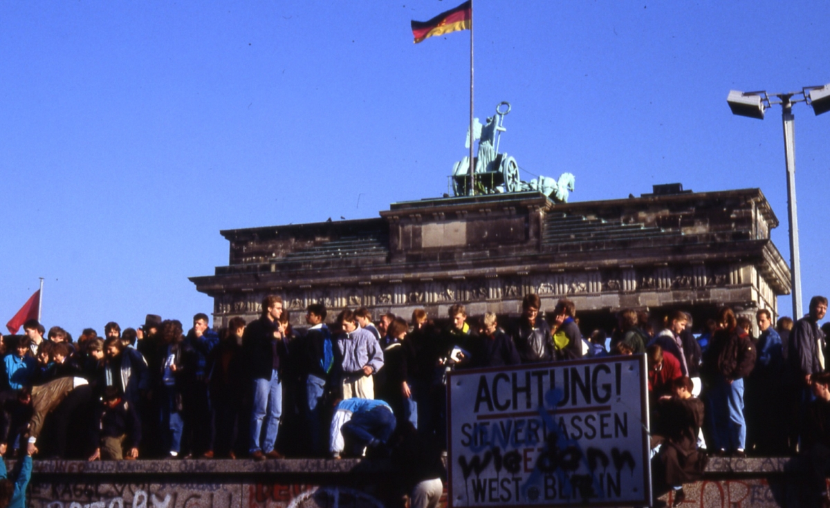 Der Mauerfall vor dem Brandenburger Tor, zahlreiche Menschen stehen auf der Mauer