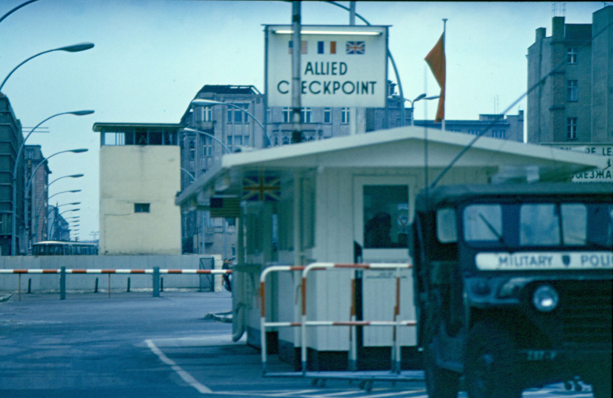 Ein Jeep der US Militärpolizei vor dem alliierten Kontrollhäuschen, rot-weiße Schlagbäume und der DDR-Wachturm.