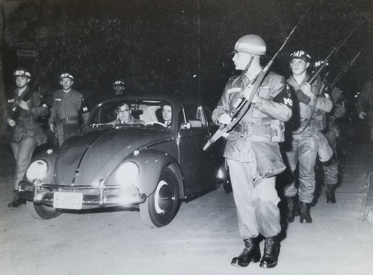 Six uniformed and armed members of the US military police accompany the Volkswagen Beetle of Edwin A. Lightner. 