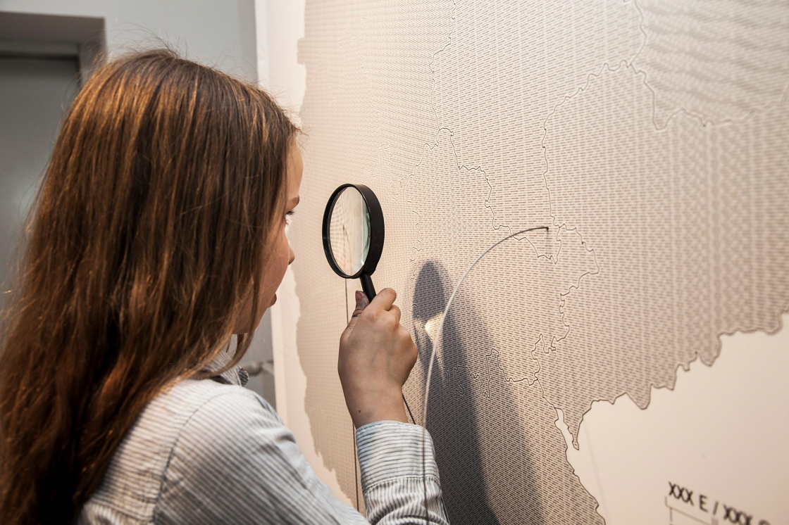A girl analyses a map section on the wall with a magnifying glass