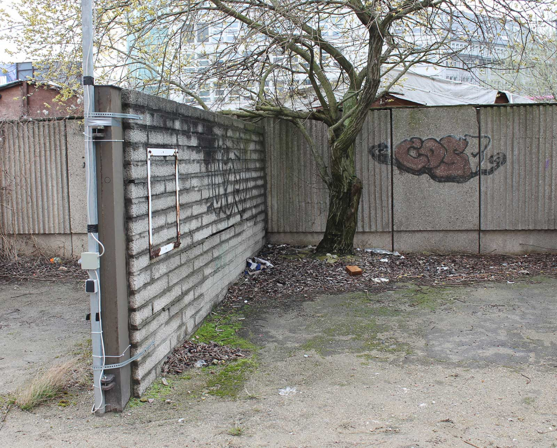Three grey wall segments made of individual concrete blocks and slabs with graffiti, next to a bare tree.