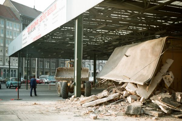 A mountain of rubble under the roof of the border crossing hall, in the background a man is walking towards a bulldozer.