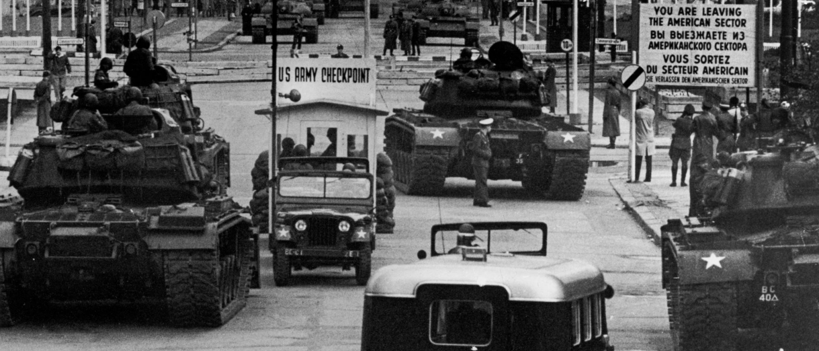 Three US tanks in front of the sign marking the sector border, with several Soviet tanks in the background on GDR territory.